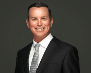 confident professional in black suit and gray tie, exuding warmth and approachability.